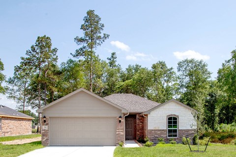 A house with a garage and a brick chimney is surrounded by trees.