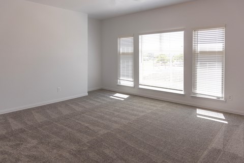 A room with a carpeted floor and three windows.