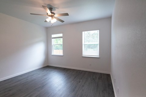 A room with a ceiling fan and two windows.