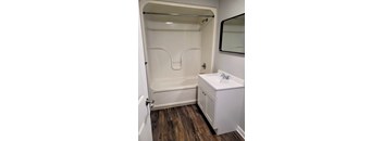 A white bathroom with a wooden floor and a white sink.