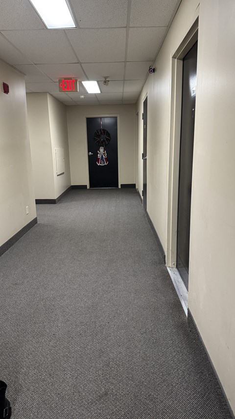 A hallway with a black door and a red exit sign above it.