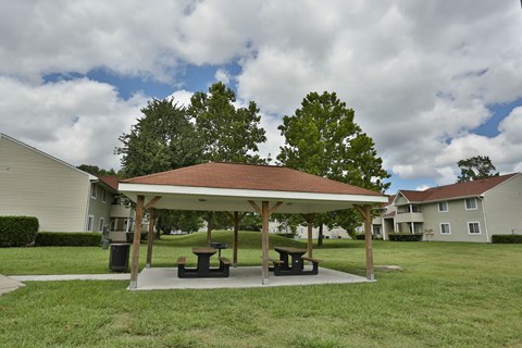 A pavilion with picnic tables is surrounded by grass and trees.