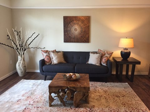 A living room with a blue couch, a wooden coffee table, and a painting on the wall.