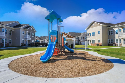 A playground with a blue slide and a brown sandbox in front of apartment buildings.