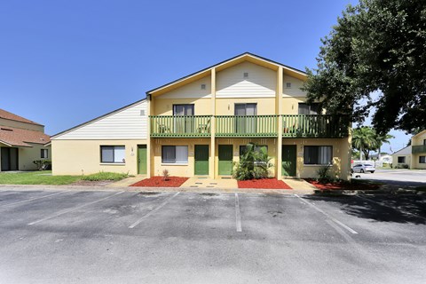 A yellow and white two story apartment building with a red mulch bed in front.
