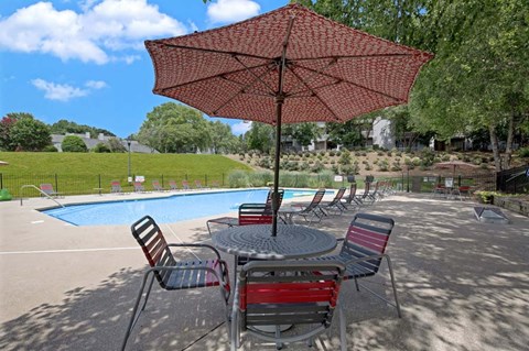 A red umbrella shades a table with chairs around a pool.