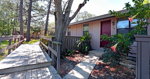 A wooden deck leads to a house with a red door.