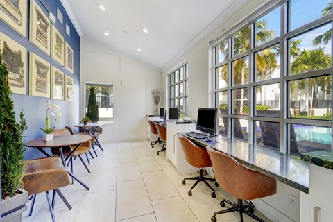 A room with a desk and chairs with a view of a pool outside the window.