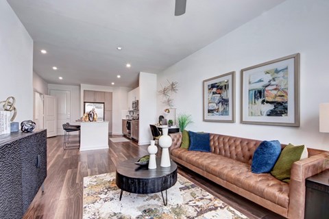 A brown couch with blue and green pillows is in the center of a room with a round coffee table.