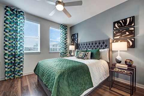 A bedroom with a bed, a ceiling fan, and a nightstand with a lamp.