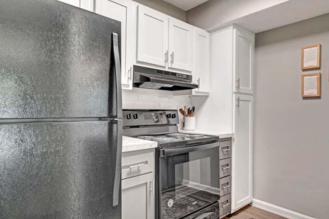 A black refrigerator stands next to a stove in a kitchen.