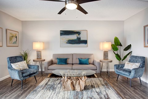 A living room with a blue chair, a white couch, and a painting on the wall.
