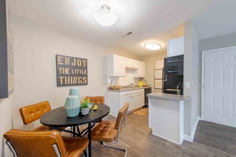 A kitchen with a dining table and chairs and a sign on the wall that says "Enjoy the little things".