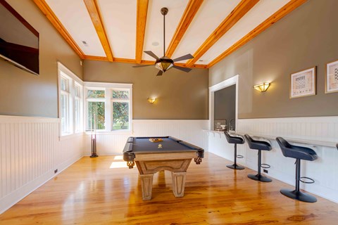 A pool table is in the middle of a room with a bar and stools.