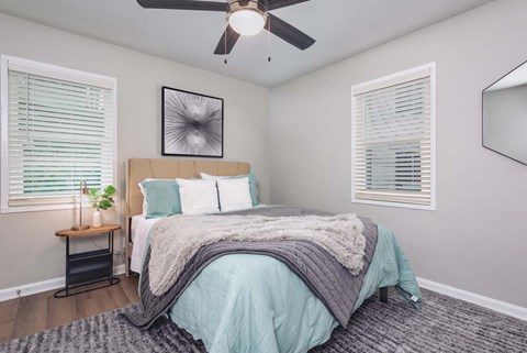 A bedroom with a bed, a ceiling fan, and a nightstand with a plant on it.