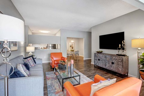 A living room with a grey couch, orange chairs, and a television.