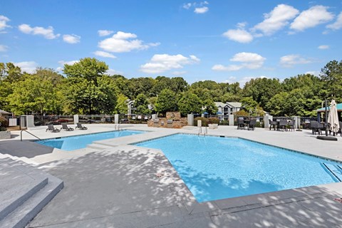 A large outdoor swimming pool surrounded by trees and lounge chairs.