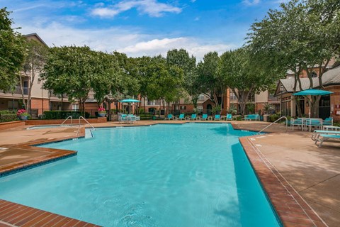 A large outdoor swimming pool surrounded by trees and lounge chairs.