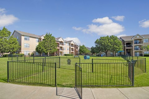 A black metal fence surrounds a green grassy area in front of apartment buildings.