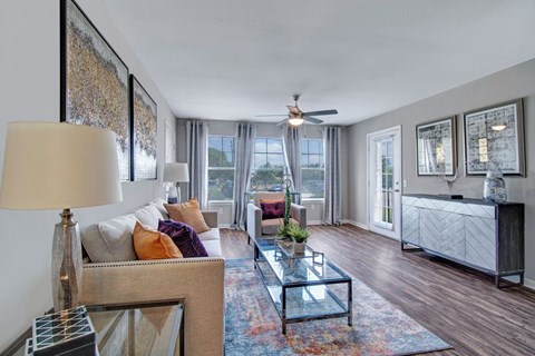 A well-lit living room with a glass coffee table and a sofa with throw pillows.