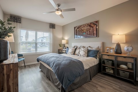 A bedroom with a bed, a ceiling fan, and a painting on the wall.