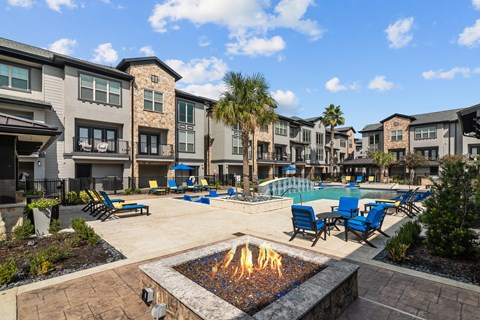A fire pit in the middle of a patio surrounded by chairs and palm trees.