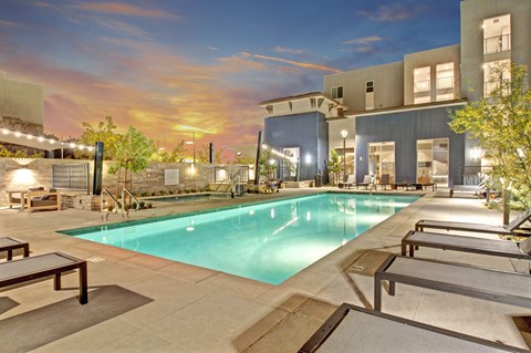 A swimming pool surrounded by lounge chairs and a building in the background.