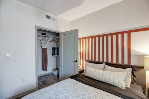 A bedroom with a large bed and a closet with clothes hanging.