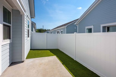 A white fence separates a concrete patio from a grassy area.
