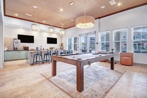 A pool table is in the middle of a room with a bar and a television.