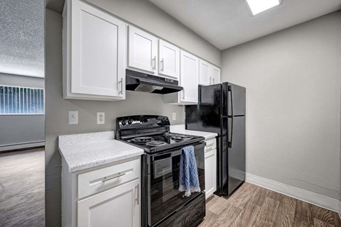A black refrigerator is in a kitchen with white cabinets.
