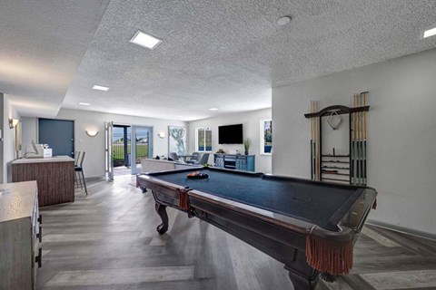 A pool table is in the middle of a room with a bar and a television.