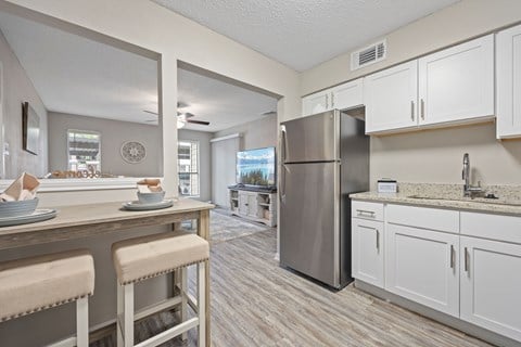 A kitchen with a refrigerator, bar stools, and a dining table.