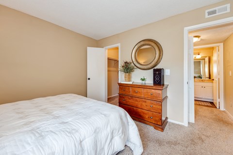 A bedroom with a white bed, a wooden dresser with a mirror above it, and a white closet.