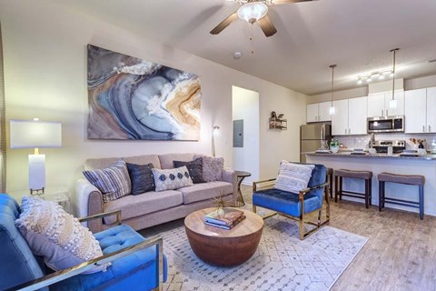 A living room with a large painting on the wall and a kitchen area in the background.