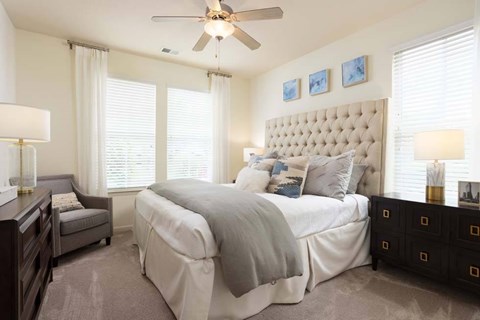 A bedroom with a large bed, a ceiling fan, and a nightstand with a lamp.