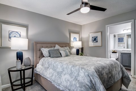 A bedroom with a bed, a ceiling fan, and a nightstand with a lamp.