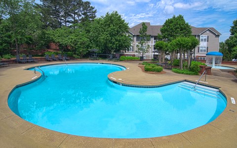 A large outdoor swimming pool surrounded by trees and a building in the background.