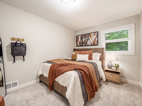 A bedroom with a large bed and a window showing greenery outside.