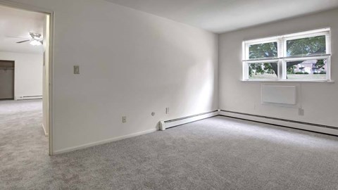A room with a carpeted floor, a window with a view of trees and a house, and a door leading to another room.