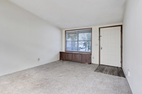 A room with a carpeted floor, a window with blinds, a wooden bench, and a white door.