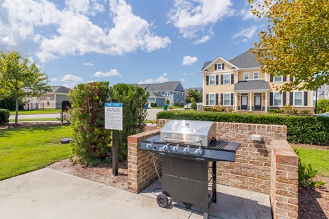 A BBQ grill is in front of a brick wall and a sign is in the background.