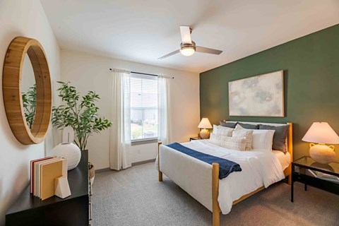 A bedroom with a bed, nightstand, and a plant.