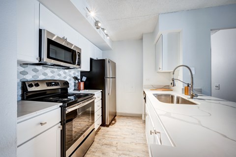 A kitchen with a black refrigerator, white cabinets, and a white countertop.