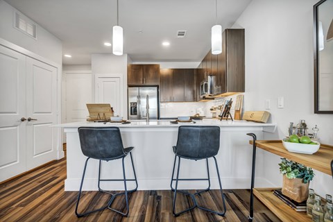 A modern kitchen with a white island and two black chairs.