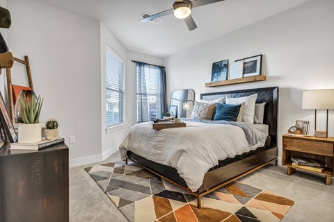 A bedroom with a bed, a rug, a nightstand, and a ceiling fan.