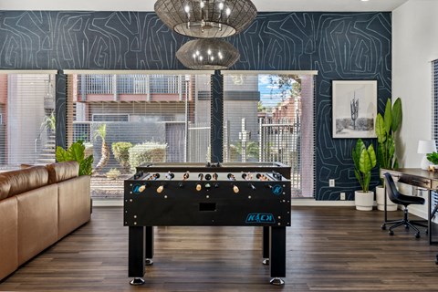 A pool table in a room with a brown leather couch and a window showing an apartment building.