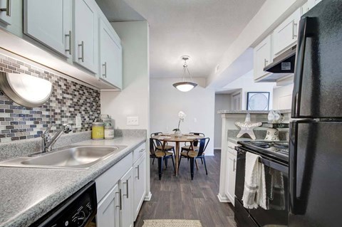 A kitchen with a black refrigerator, a sink, and a dining table with chairs.