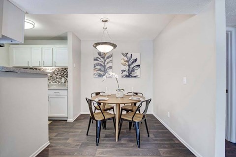 A dining room with a table set for two and a kitchen in the background.