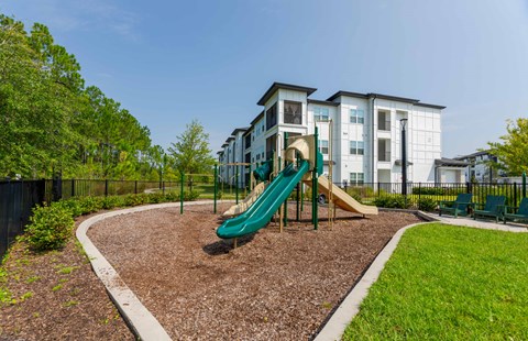 A playground with a green slide in front of a white building.